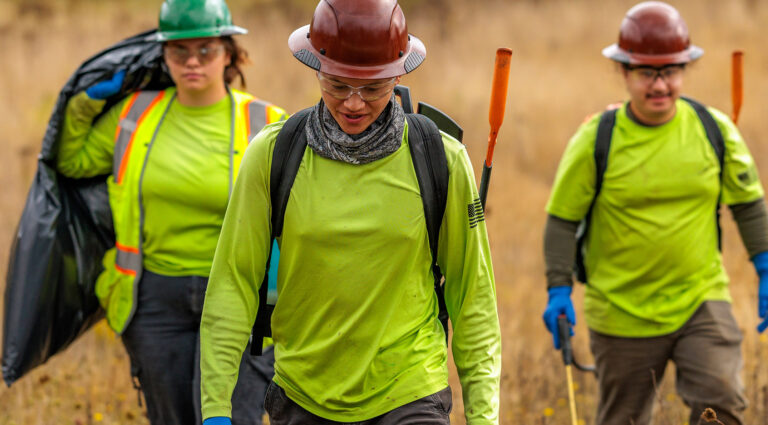 Three workers with equipment and safety gear walking through an area needing environmental permitting