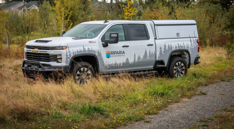 A logoed Riparia Environmental truck parked along an gravel service road
